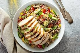 A plate of grilled lemon herb chicken served with a fresh quinoa salad with vegetables